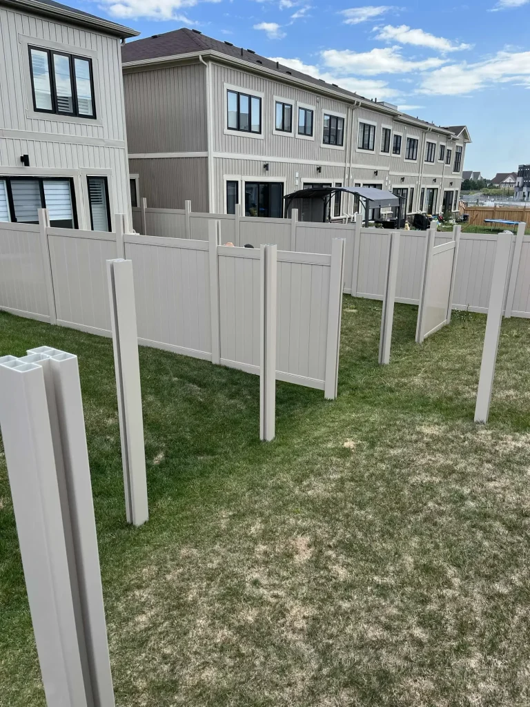 Professional crew installing a beige vinyl fence in Bowmanville, showing the precise post-setting and assembly process.