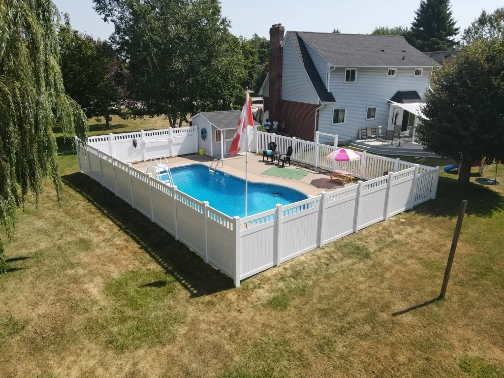 White vinyl pool safety fence installed in the far corner of a residential backyard in Bowmanville, Ontario.