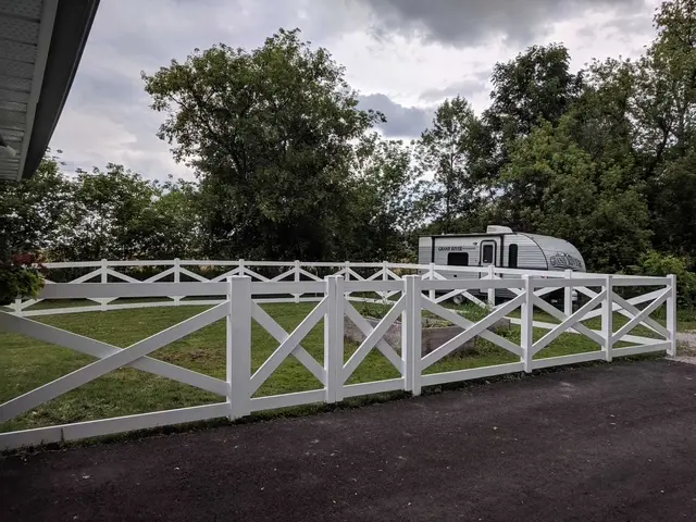 Wide-angle view of a white vinyl ranch fence bordering a rural dirt road in Ontario.